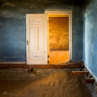 Warm, morning lights pours into an abandoned building in Kolmanskop where a door sits halfway up a wall