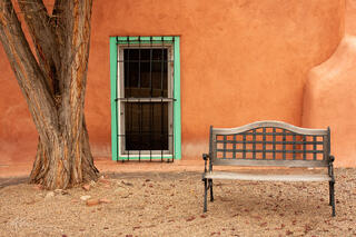 Adobe building with turquoise window frame, tree and bench