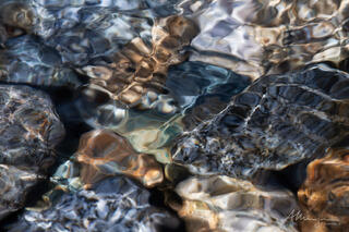 sunlight in shallow water with colourful river rocks