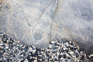 rocks eroded by pounding wave action to make smooth pebbles sit at the base of larger igneous rock on the Pacific Northwest coastline in British Columbia