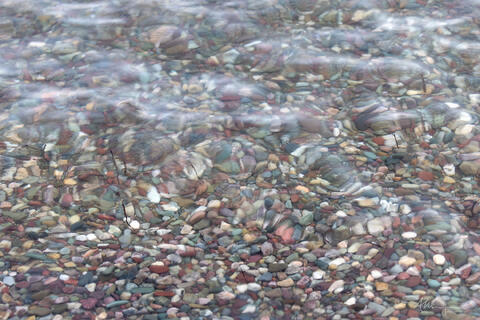water flowing over multicoloured rocks at lake edge causing the rocks to appear distorted.
