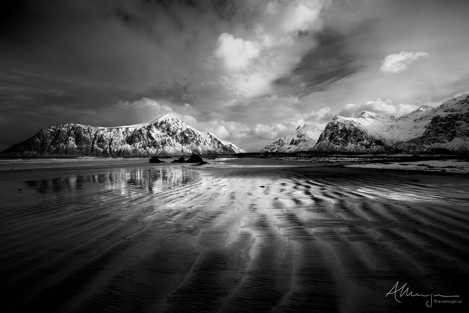 Black and white sand on a Norwegian beach form dramatic line patterns.  Snow capped mountains add to the drama